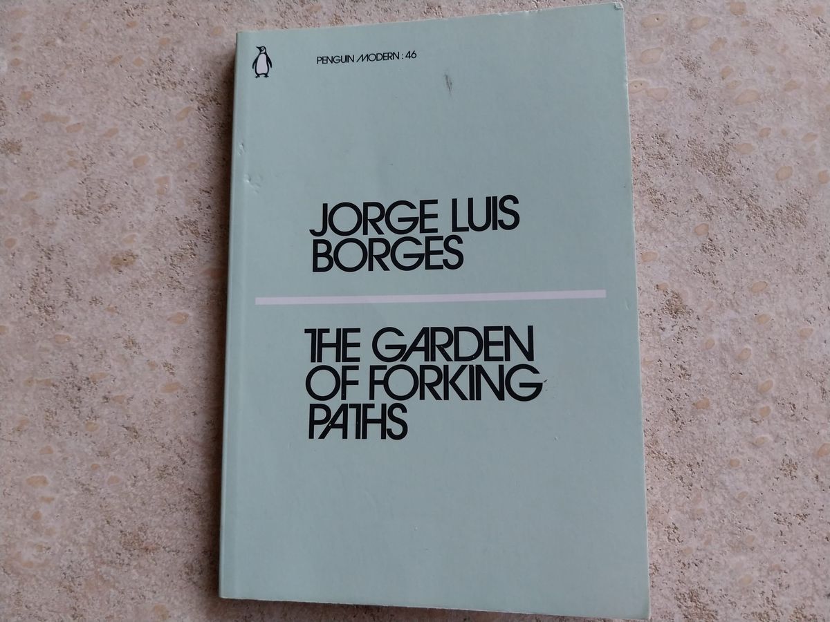 On a concrete background, a light-blue book. The book is The Garden of Forking Paths by Jorge Luis Borges.
