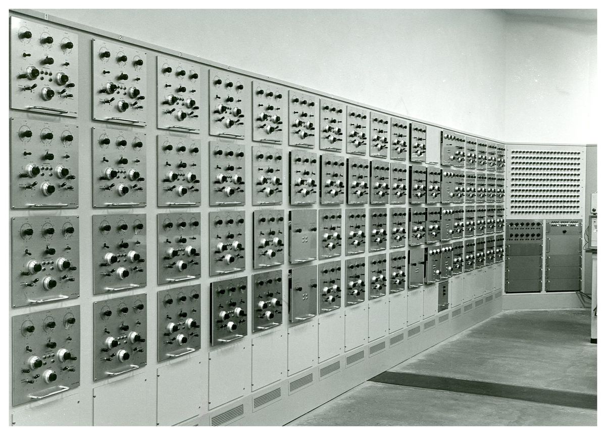 A black and white photo of a wall with a series of metal panels fitted into it. Each panel has several switches and buttons.