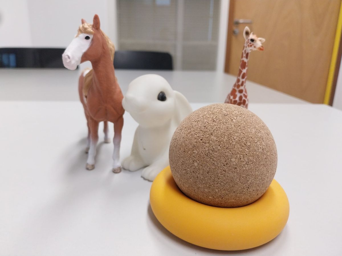 Items on a table: a toy horse, a stylized plastic rabbit, a toy giraffe. In the foreground, a ball made of cork, nestled in a yellow grip-training ring.