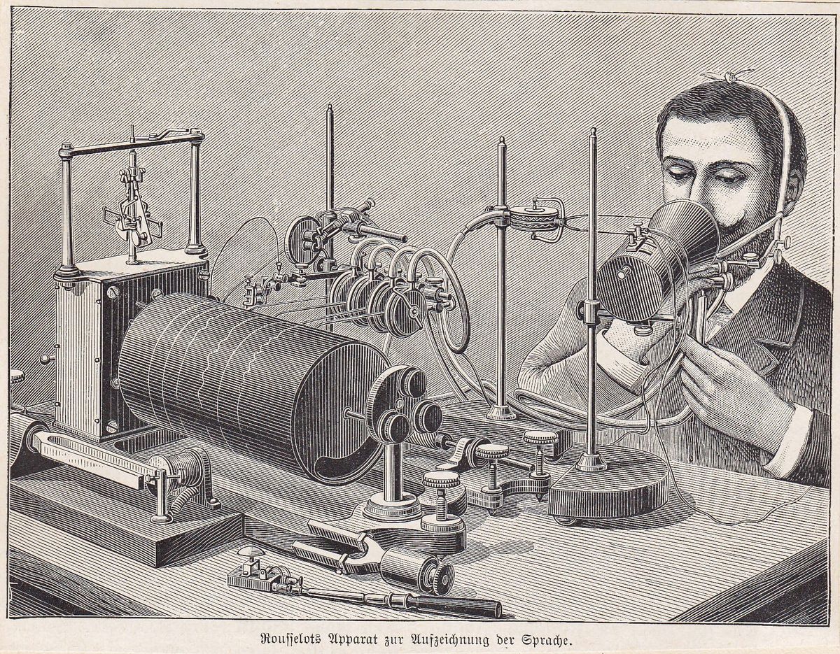Woodcut illustration of a man speaking into an old-fashioned microphone which is connected up to a mechanical needle recording sound waves on a drum.