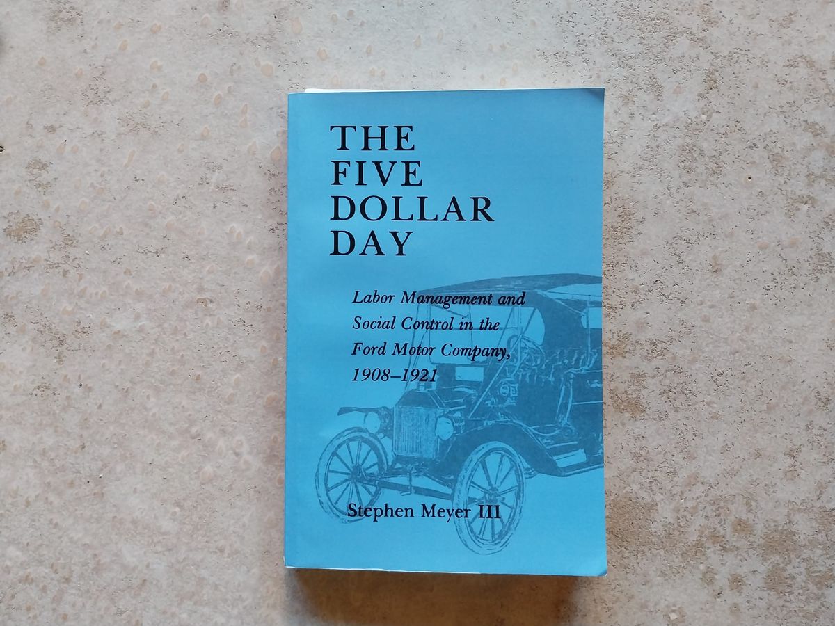 A blue book on a concrete floor. The book is The Five Dollar Day by Stephen Meyer II. The cover is simple, with an illustration of a Model T Ford.