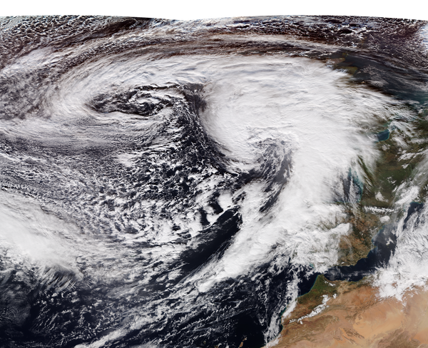 Overhead view of a storm, with clouds swirling in the foreground, and water and land in the background.