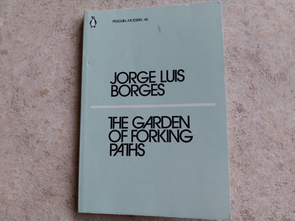 On a concrete background, a light-blue book. The book is The Garden of Forking Paths by Jorge Luis Borges.