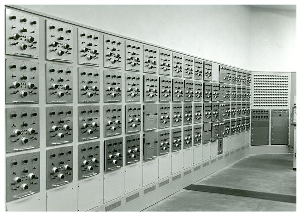A black and white photo of a wall with a series of metal panels fitted into it. Each panel has several switches and buttons.
