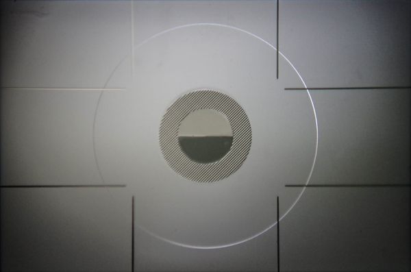 Image of a camera viewfinder without a lense. It is predominantly grey, and the centre of the image is occupied by a series of concentric circles.