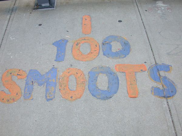 On a sidewalk, bubble writing in blue and red which reads "100 SMOOTS."