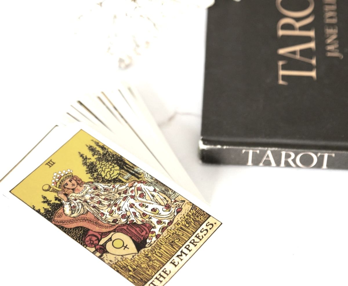 An open, somewhat splayed deck of Rider-Waite tarot cards sits on a marble table next to a black book labeled "TAROT"