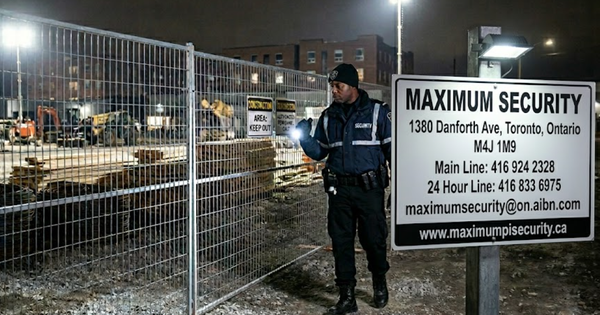 A professional commercial security guard conducting a perimeter fence inspection under high-intensity LED floodlights at a commercial construction site in Scarborough overnight.