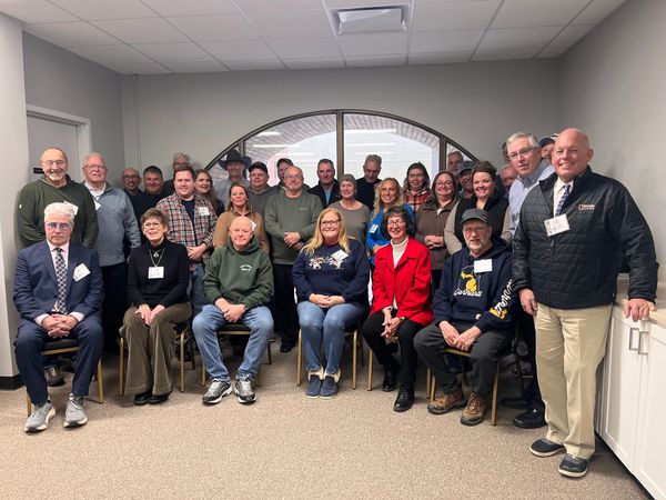 Three rows of people, some seated, pose for a picture in front of an arced window.