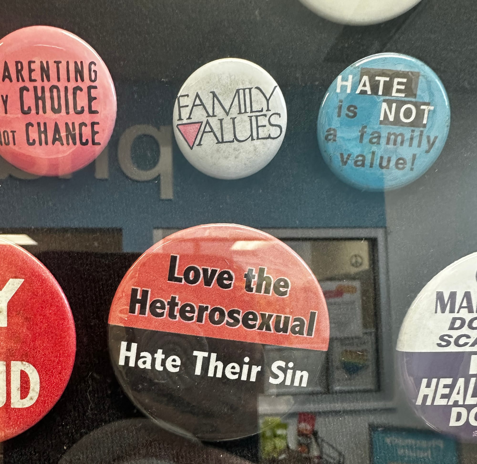 An assortment of pins with slogans: "Love the Heterosexual Hate Their Sin", "Hate is not a family value", "Family Values" (with the V replaced by a pink triangle, and "Parenting by Choice not Chance"