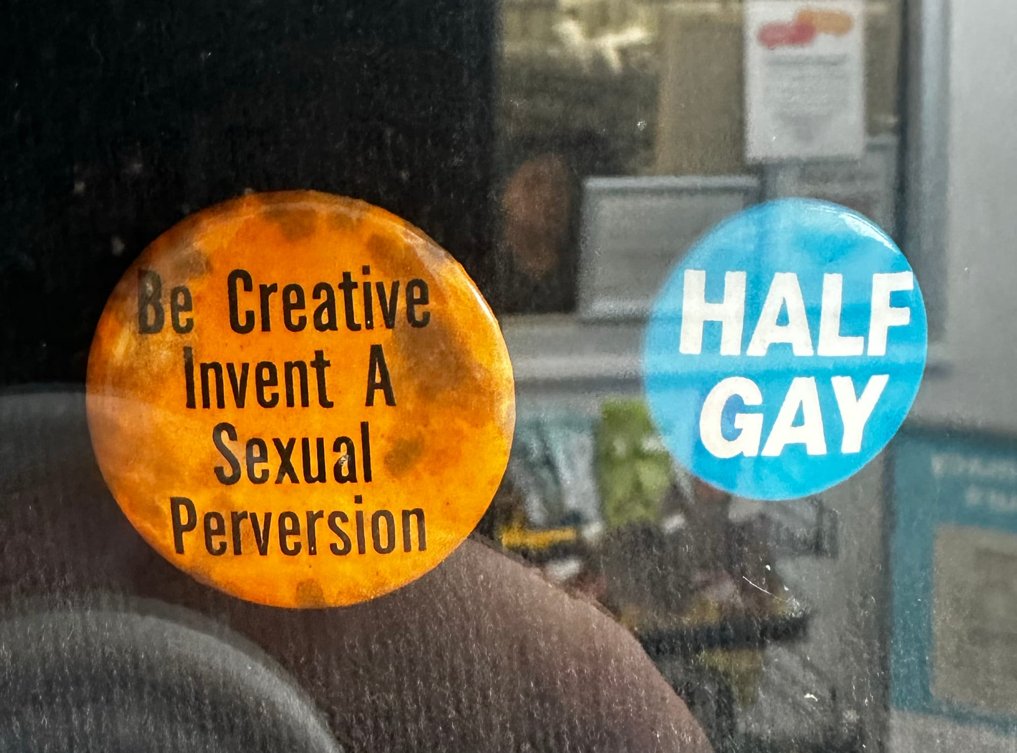 Pins reading "Be Creative Invent A Sexual Perversion" and "HALF GAY"