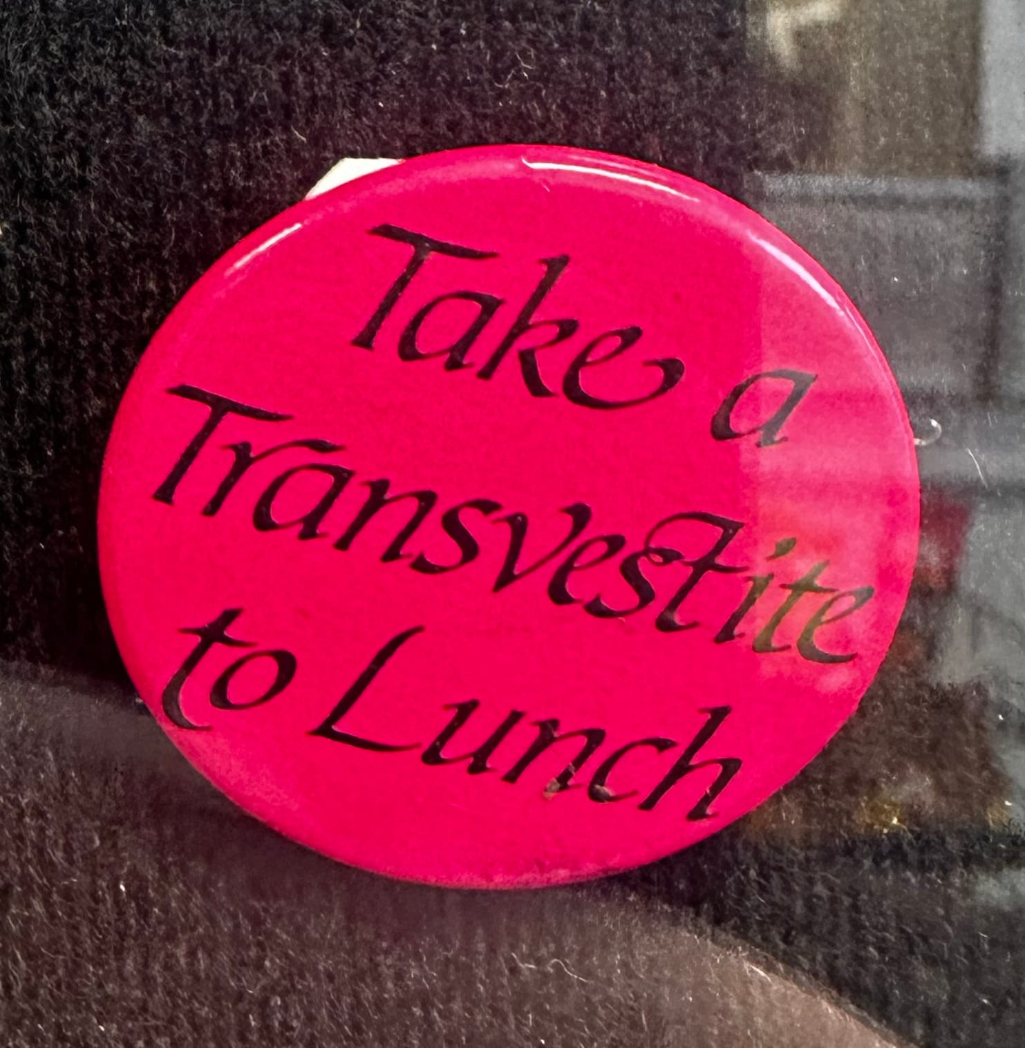 A pin reading "Take a Transvestite to Lunch"