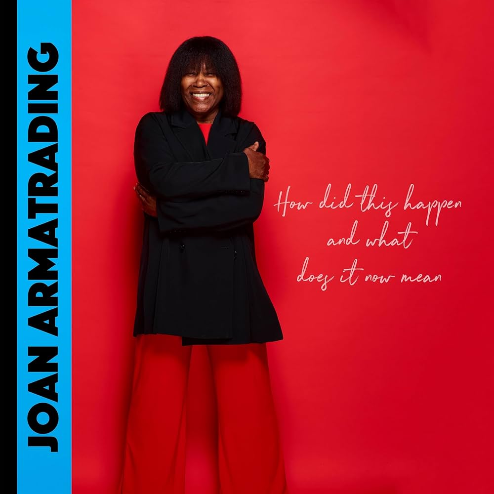 The cover of Joan Armatrading's "How Did This Happen and What Does It Now Mean" depicting the singer in a black and red outfit on a red background with her name in black on a blue background