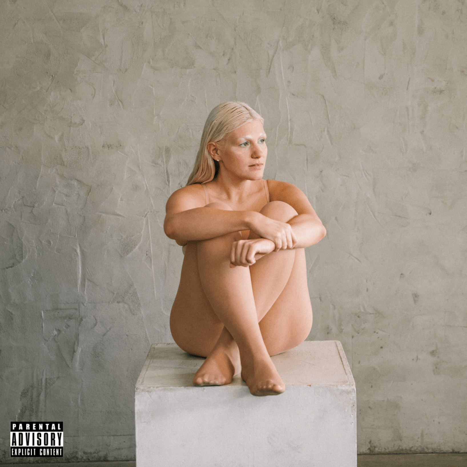The cover of Maddie Zahm's "(the angry part)" depicting the singer sitting in her underwear on a block, as if modeling for an art class. Her hair and eyebrows are bleached.