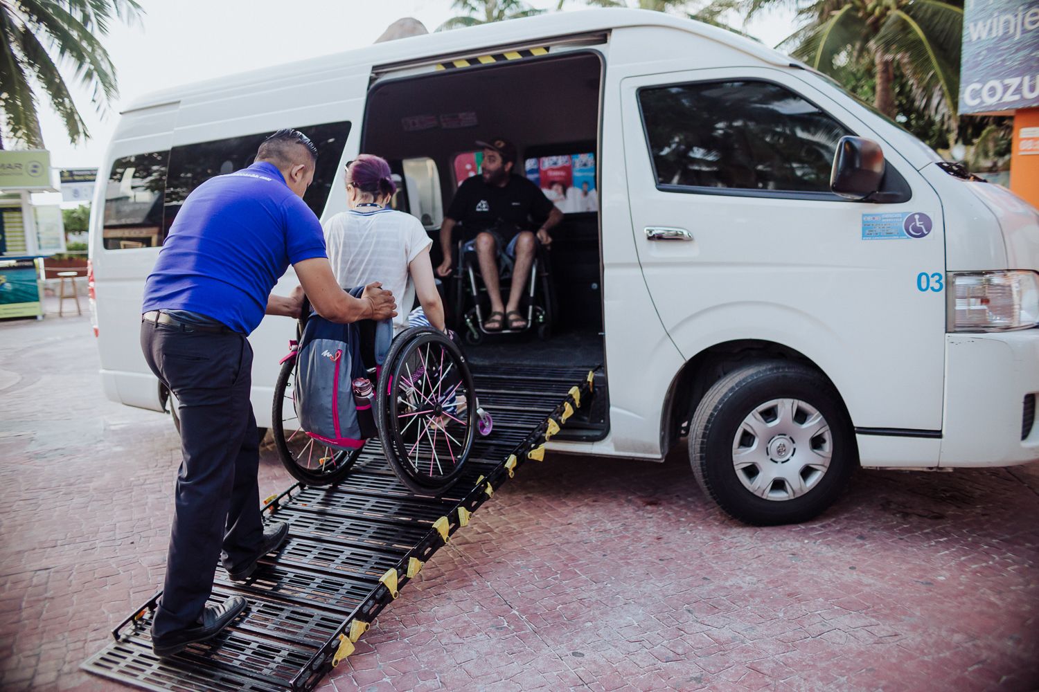 A wheelchair user entering a van with a ramp and assistance