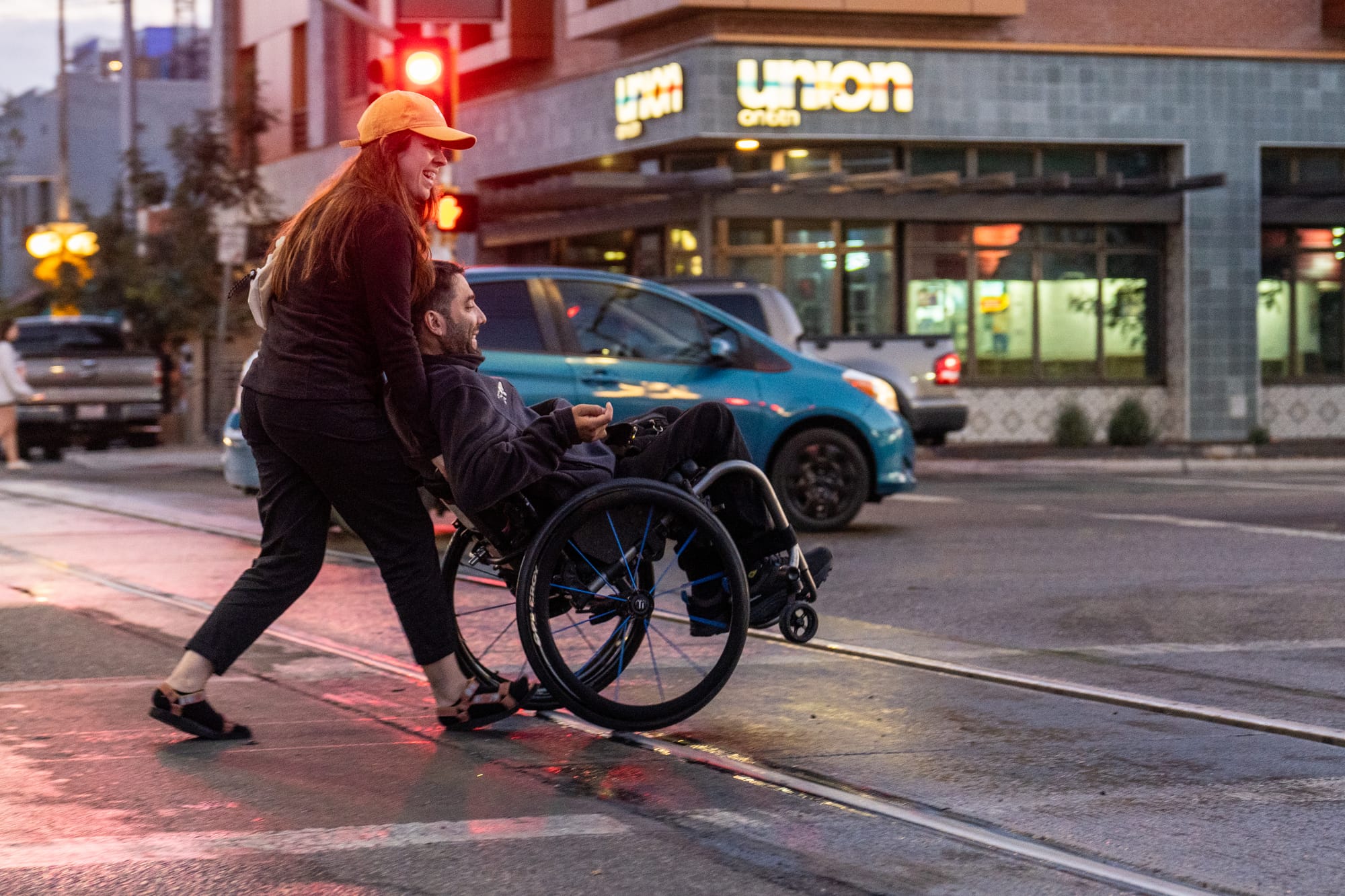 Wheelchair user and companion rolling across the street, laughing and having fun