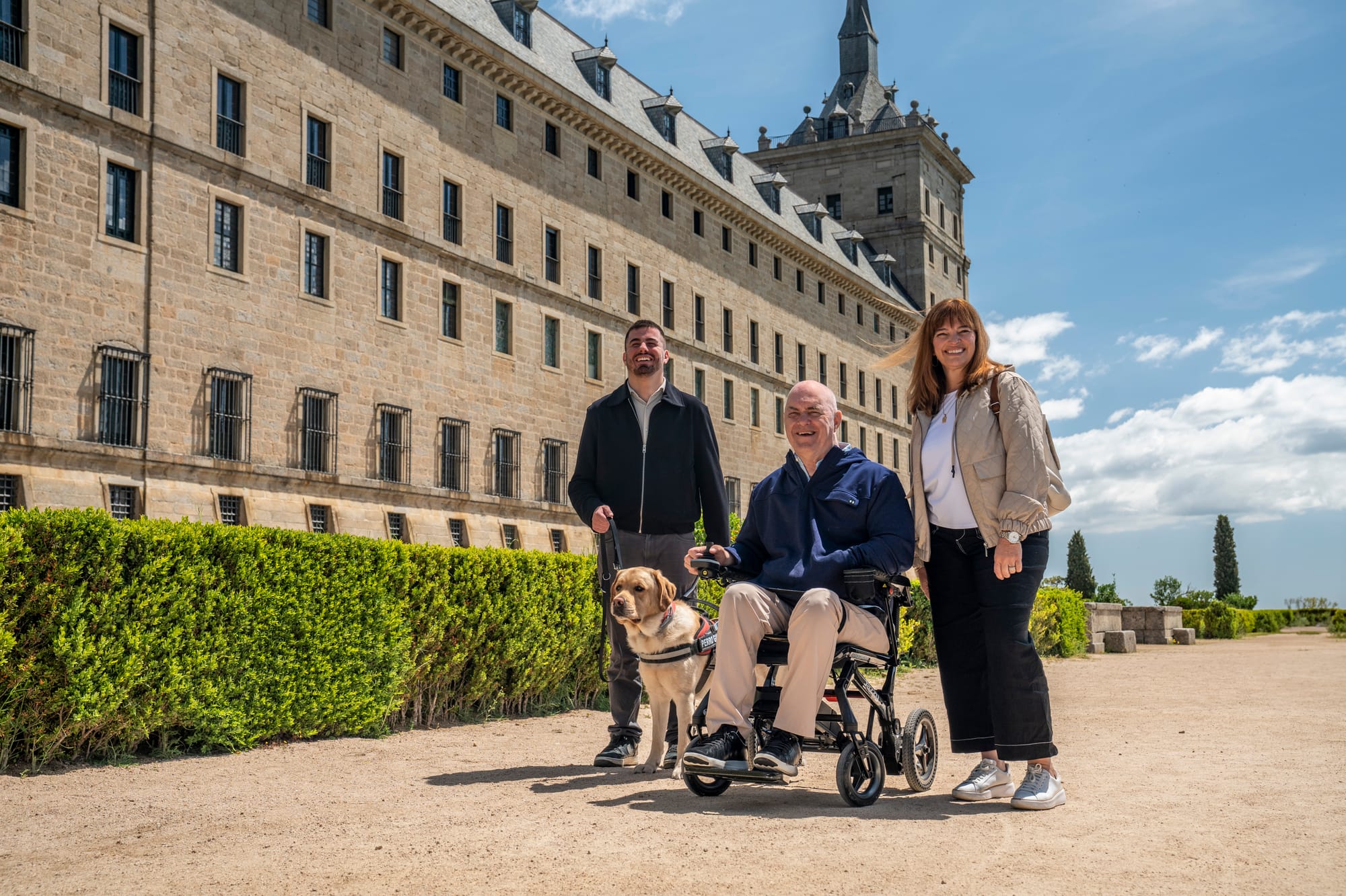 Wheelchair user, companion and blind man walking through gardens at San Lorenzo de El Escorial