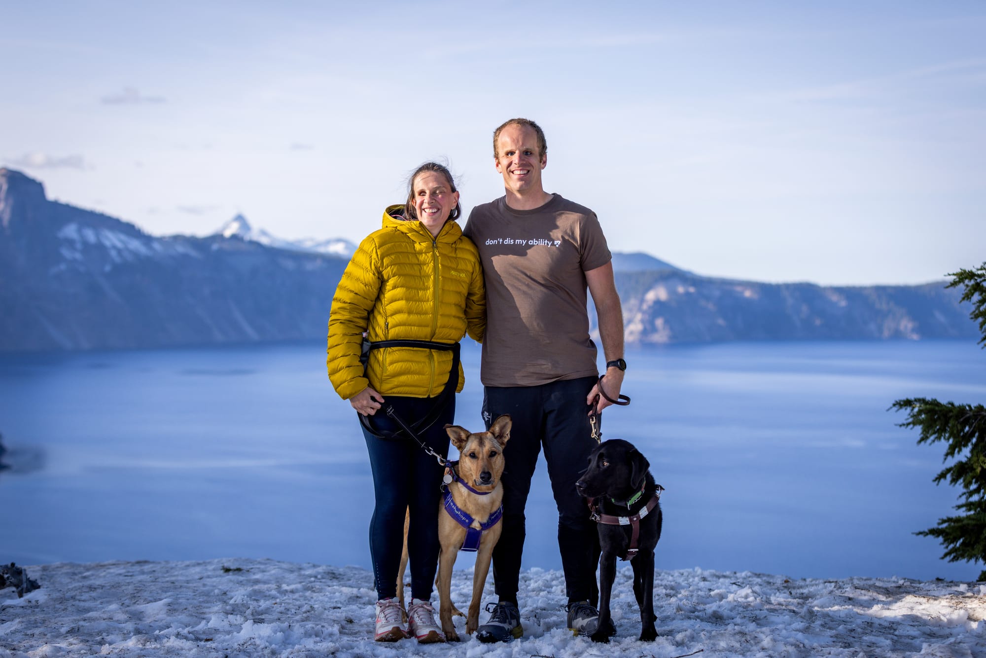 Blind couple with service dogs posing for a photo with Crater Lake in background
