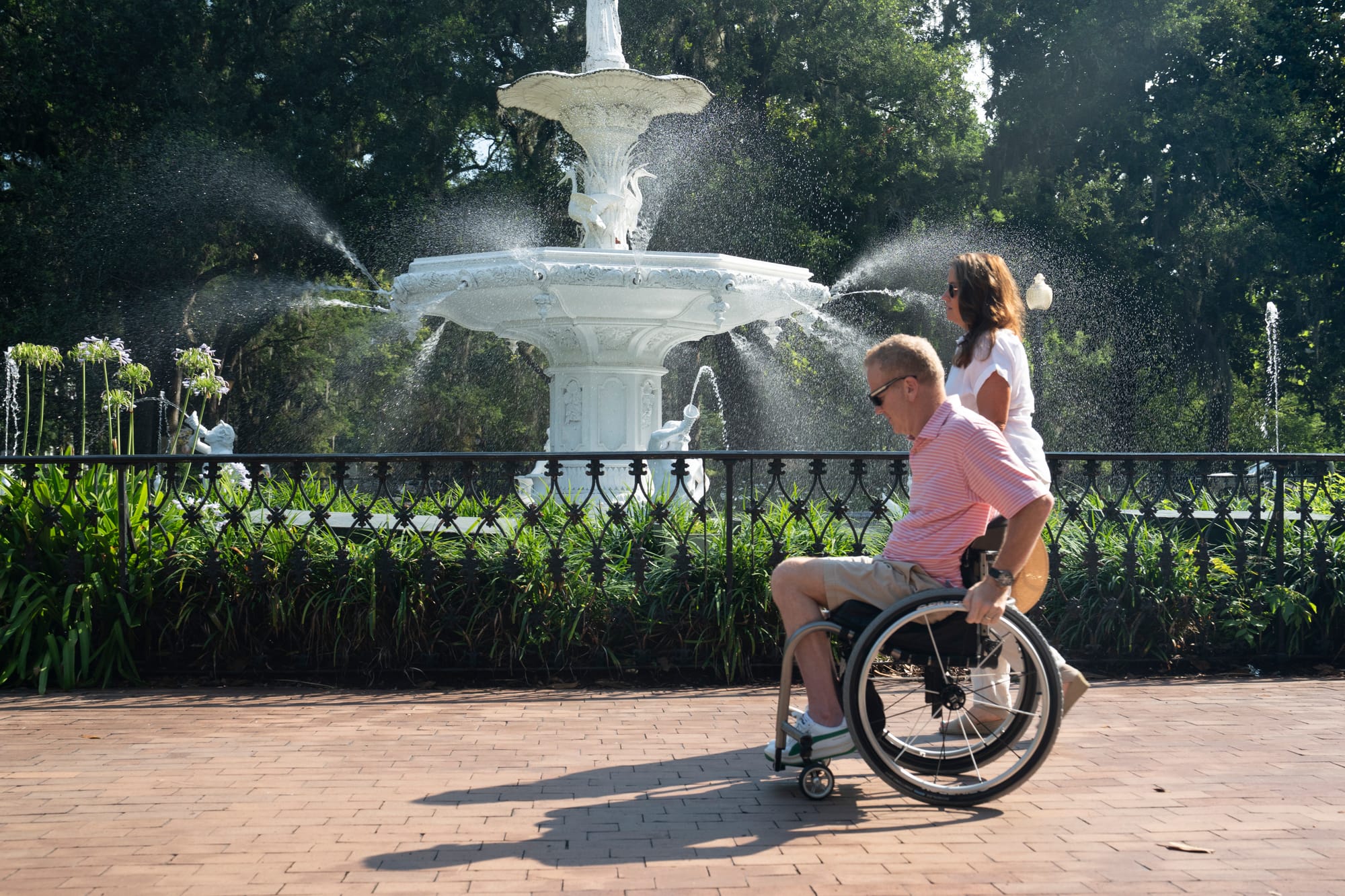 Wheelchair user and companion rolling past Fountain at Forsyth Park