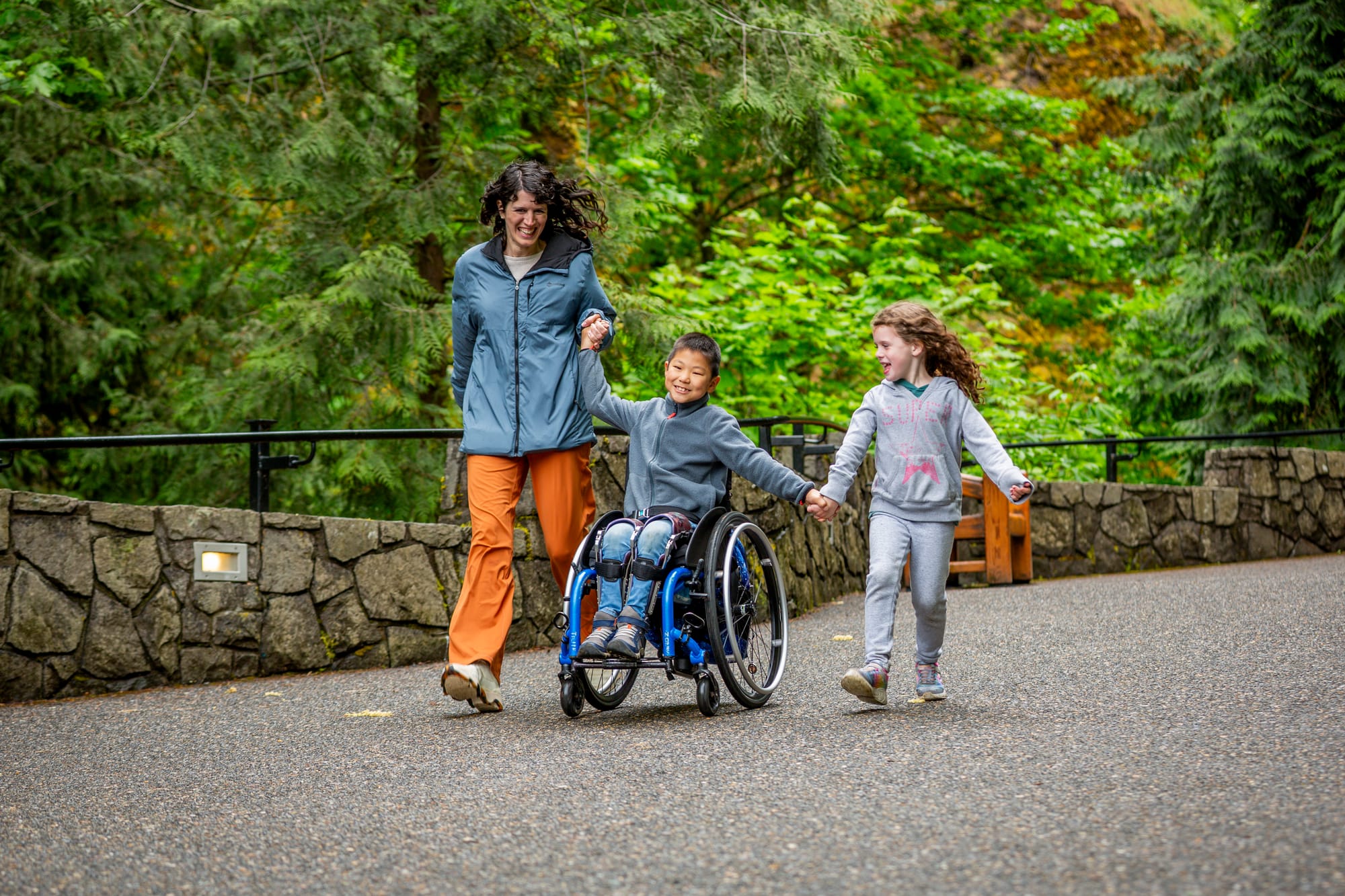 Jaden, a boy in a wheelchair and his mom and sister running down a trail at Multnomah Falls