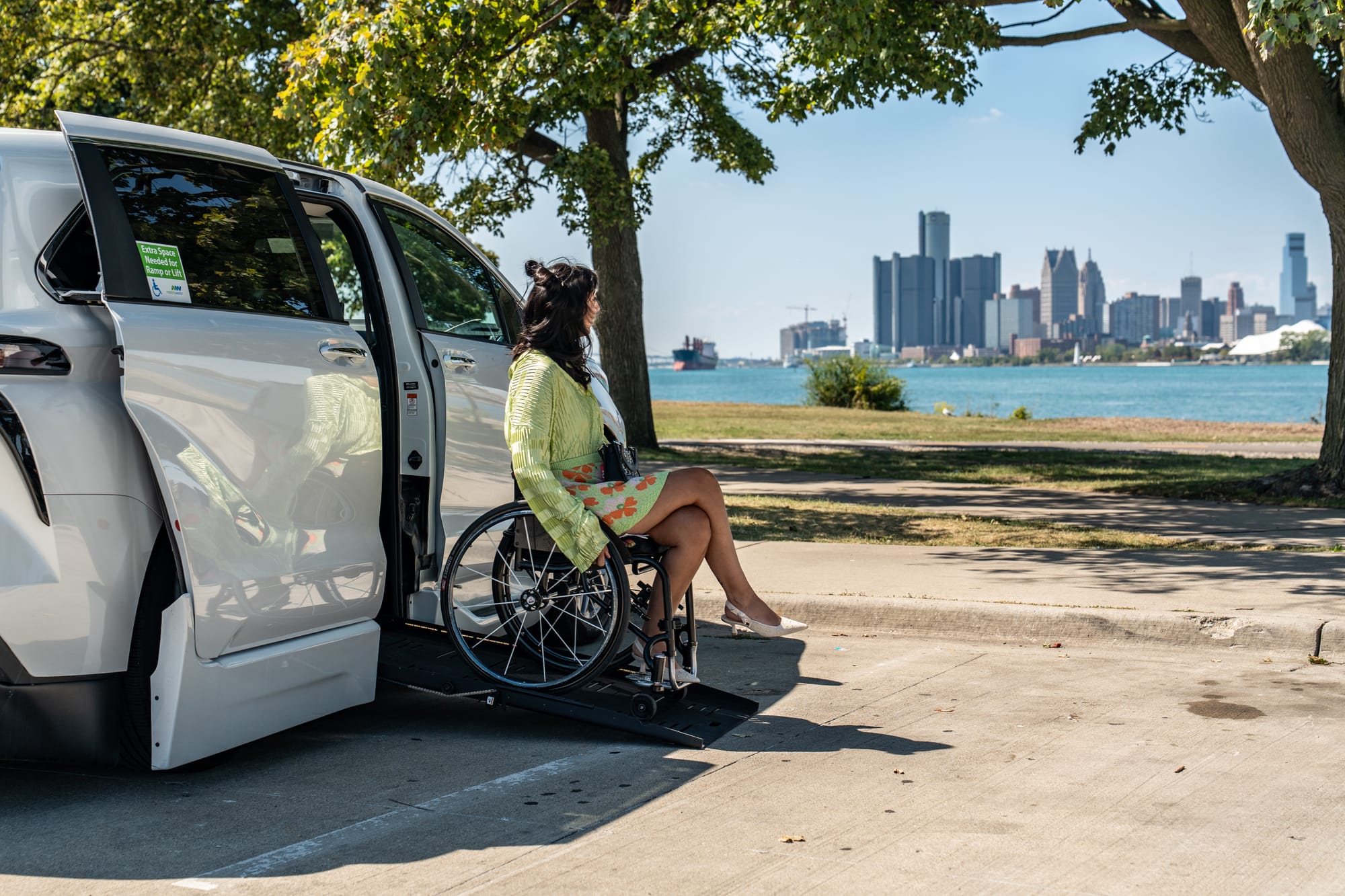 Wheelchair user exiting adapted vehicle ramp with Detroit in the background