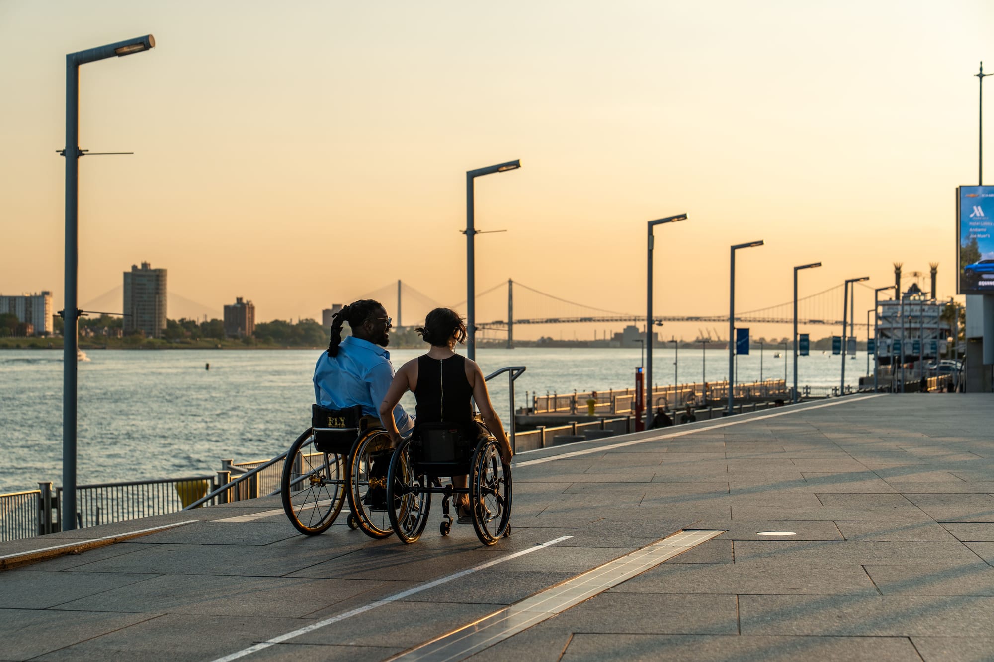 Matt Scott and Kaylee Bays, two wheelchair users on the Detroit Riverwalk at sunset