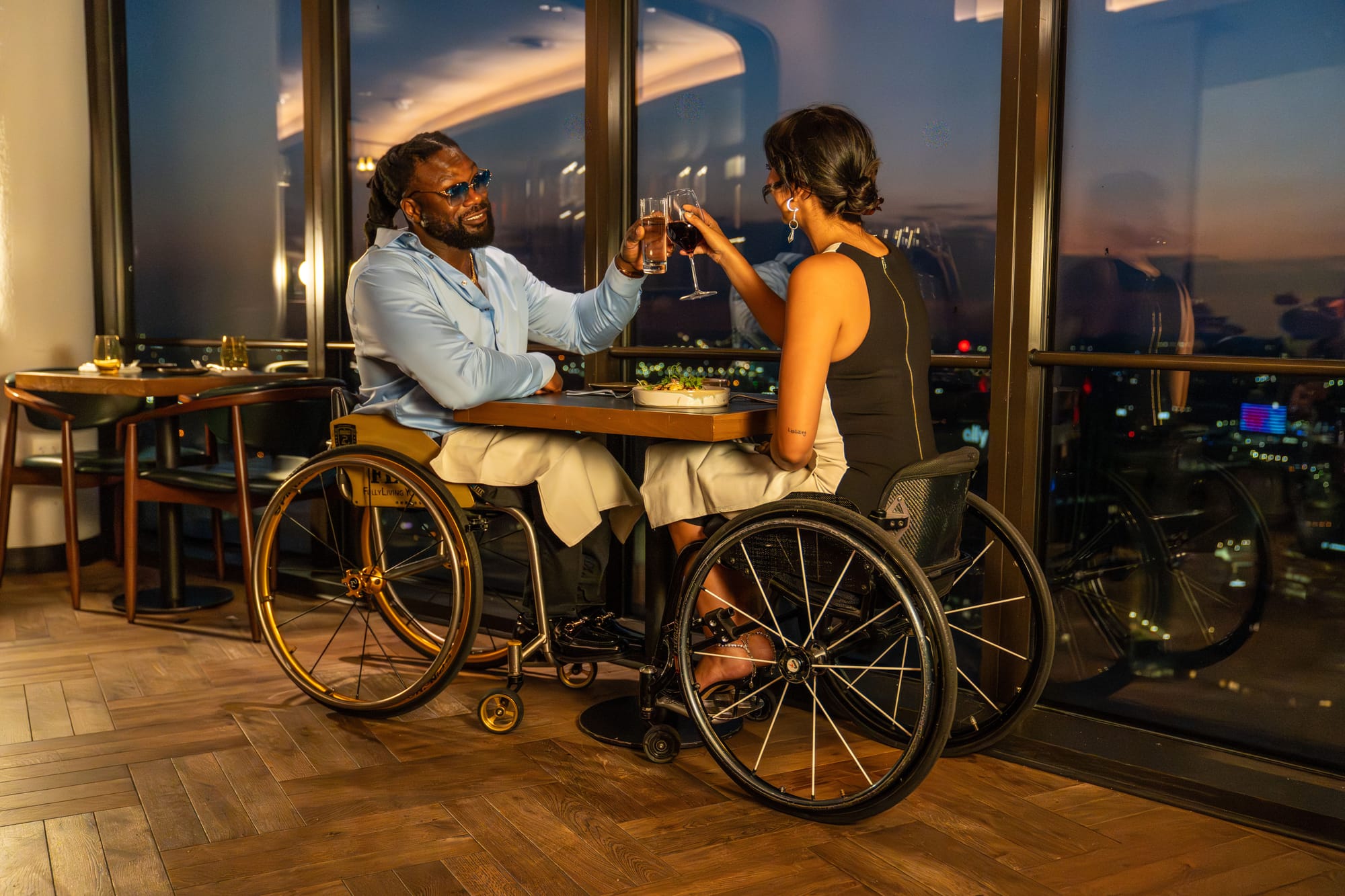 Matt and Kaylee, two wheelchair users, cheering glasses at Highlands Detroit