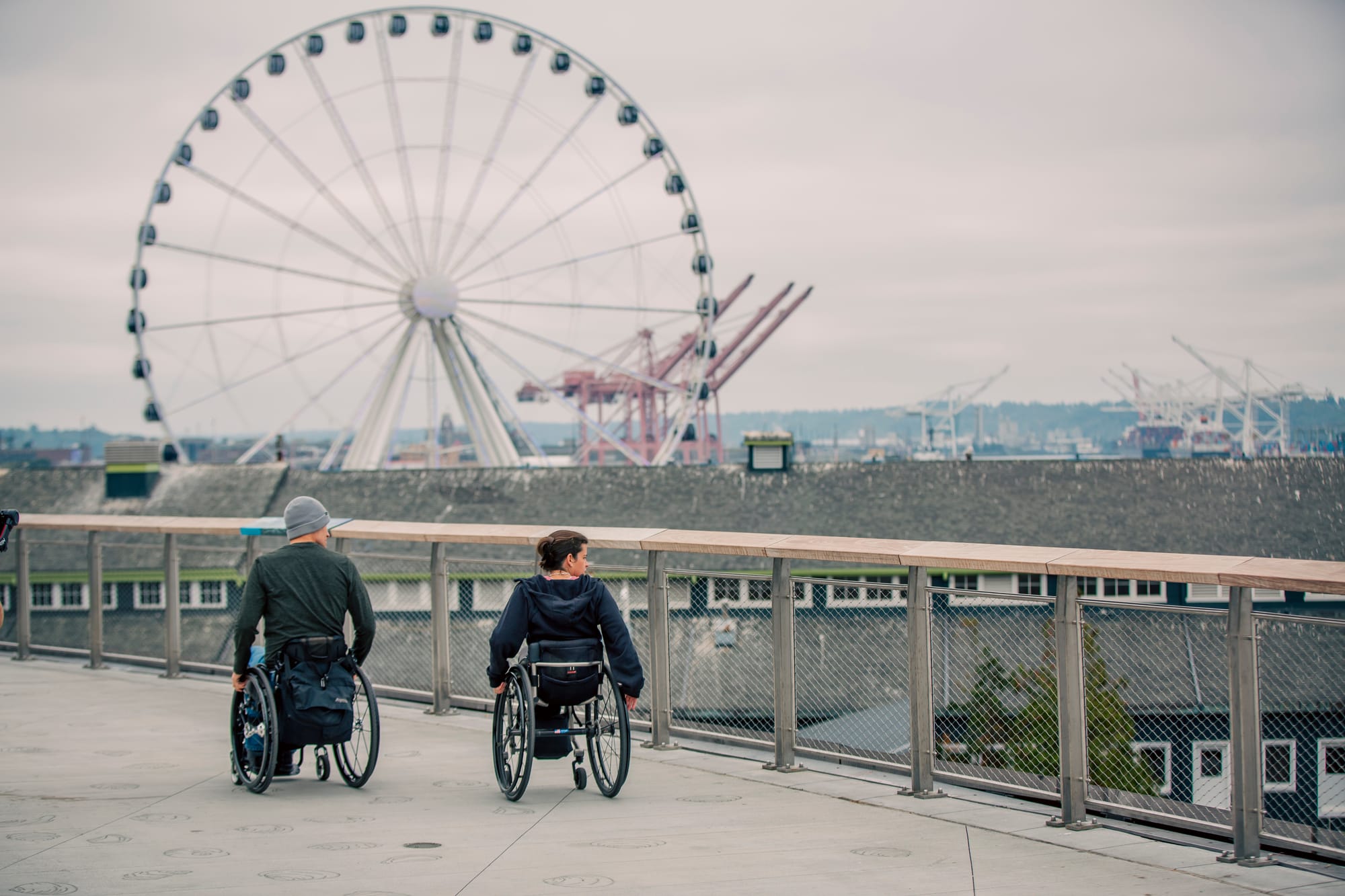 Two wheelchair users exploring Seattle with Great Wheel in the background