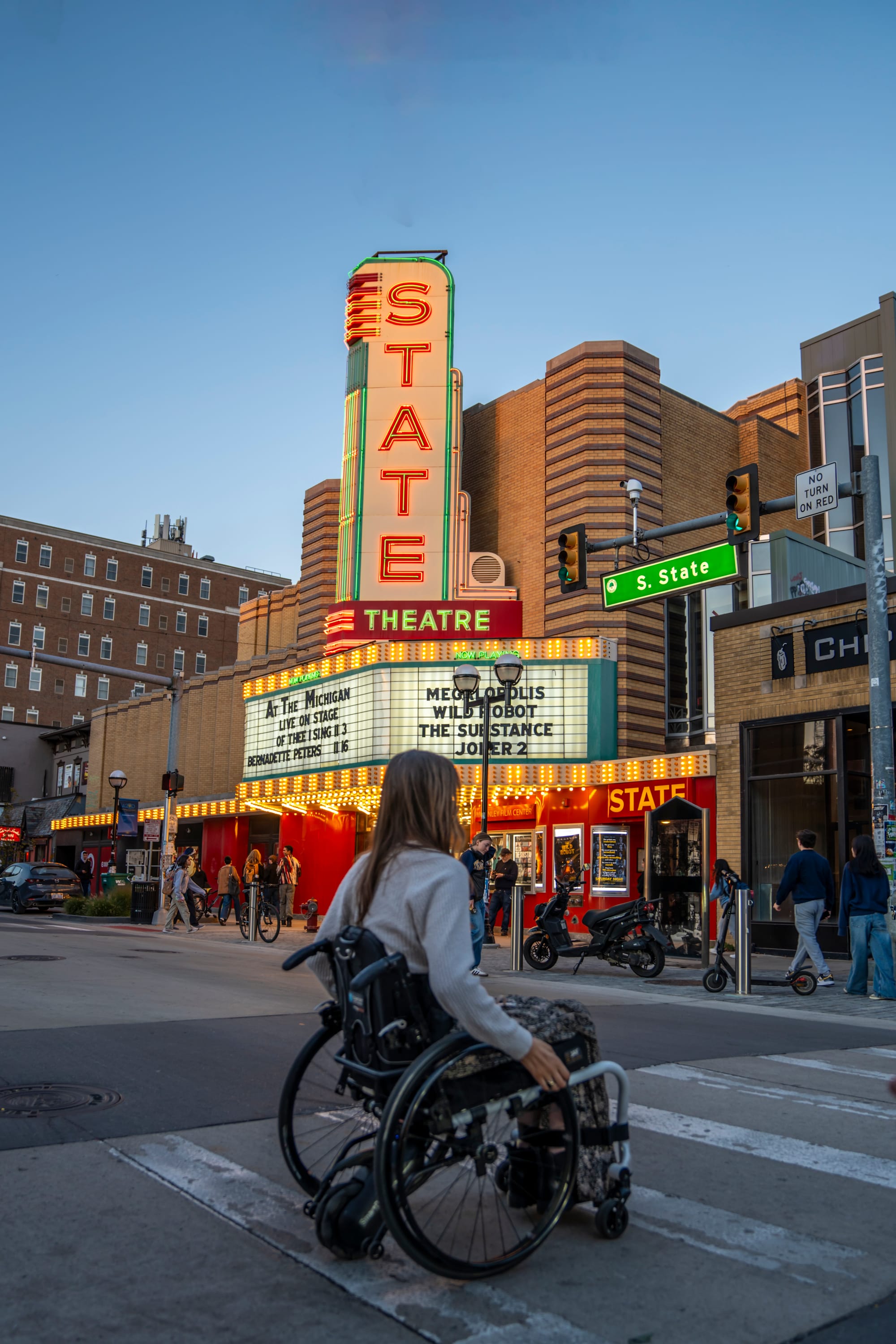 Wheelchair user crossing the street with State Theatre in the background, in Ann Arbor