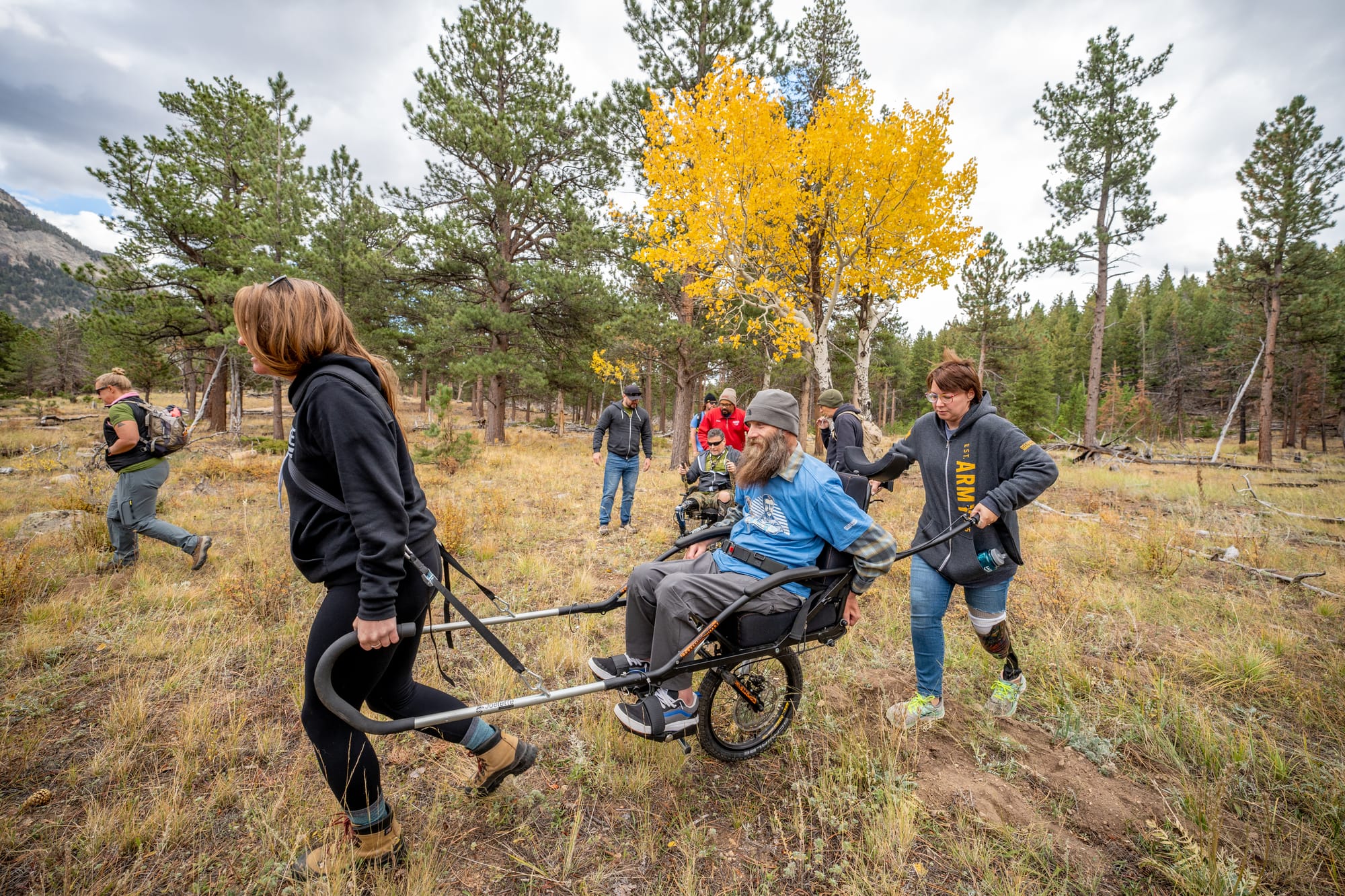 Man on Joelette wheelchair in nature with companions assisting