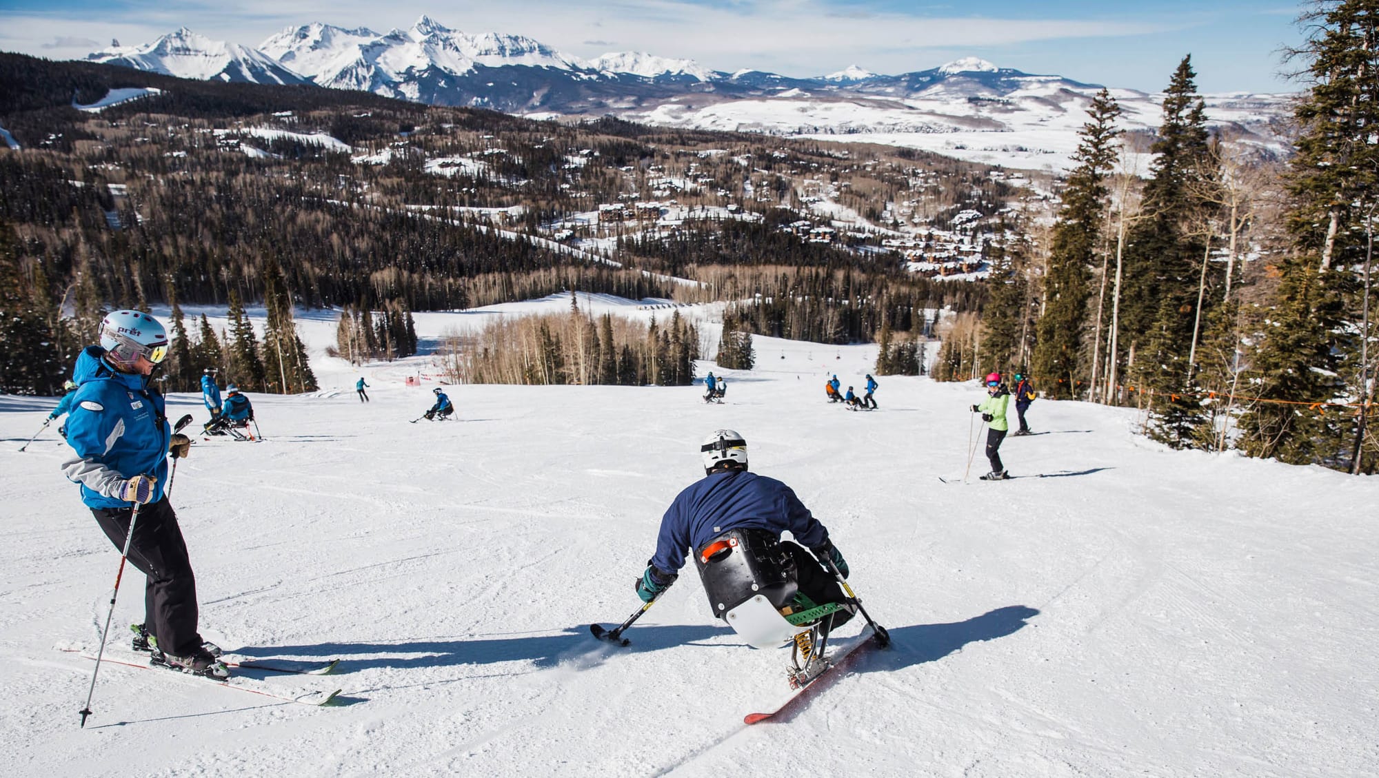 Man on an adaptive sit-ski going down the slopes with instructor beside him