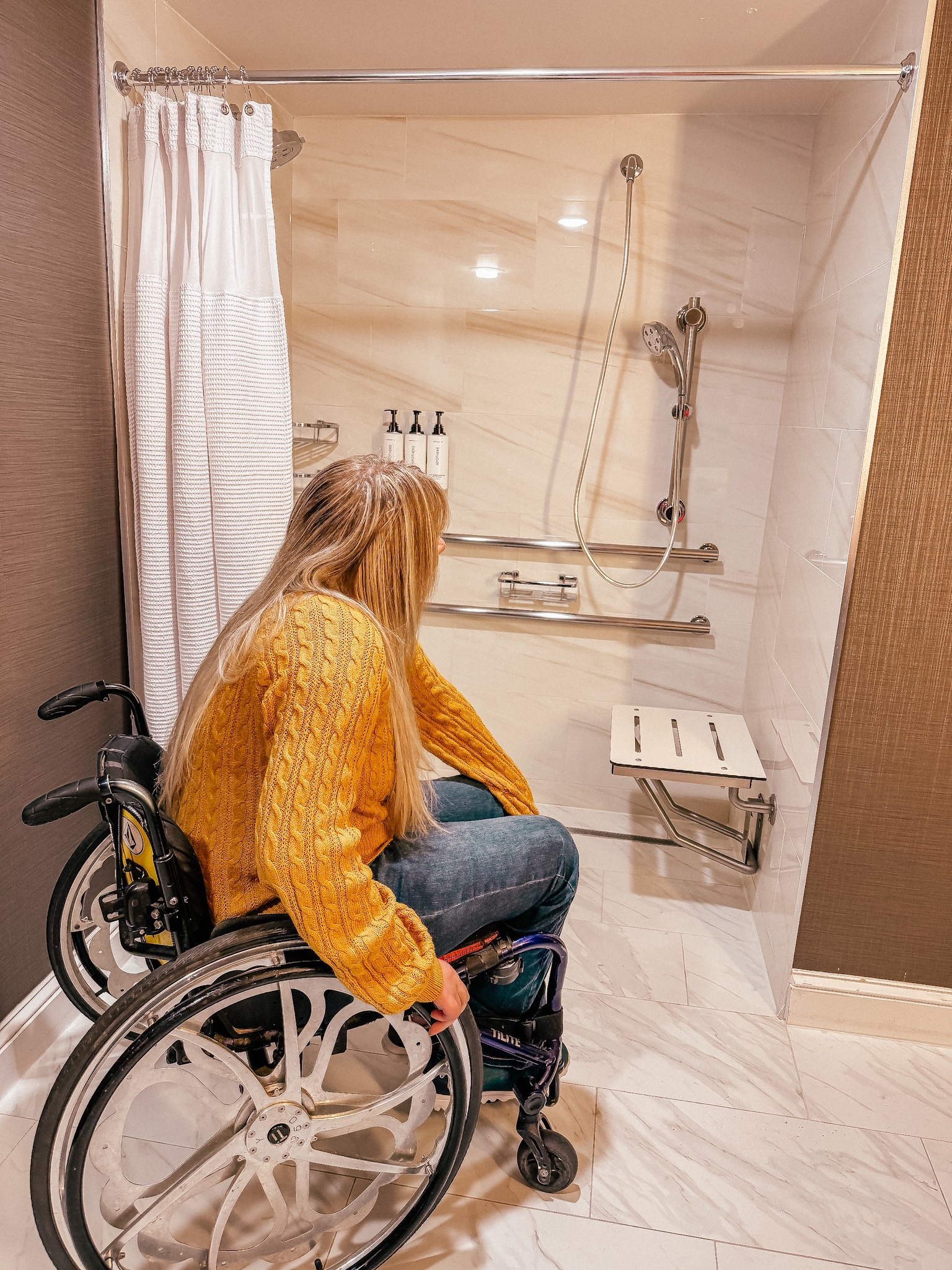 Wheelchair user in her hotel room bathroom looking at the roll-in shower