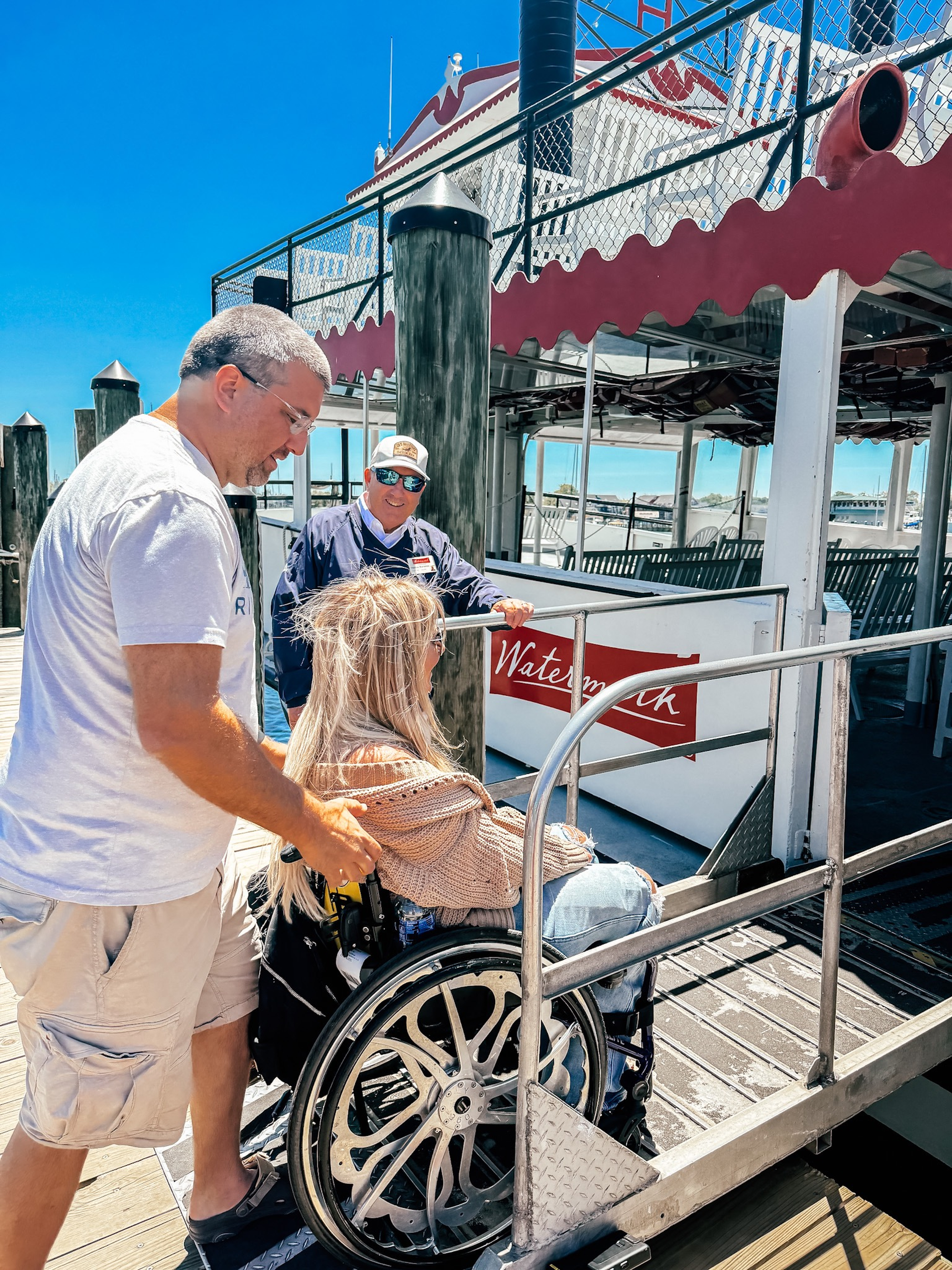 Man helping wheelchair user board a cruise boat with a ramp
