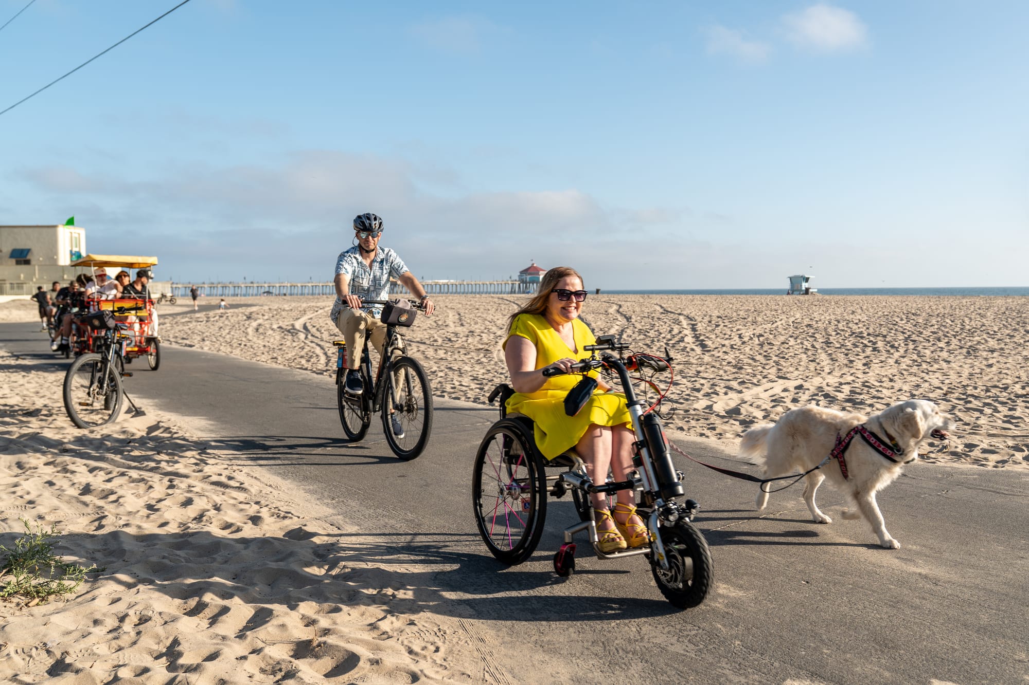 Wheelchair user strolling along Huntington Beach Ocean Bike Path with her dog, and her husband on a bike