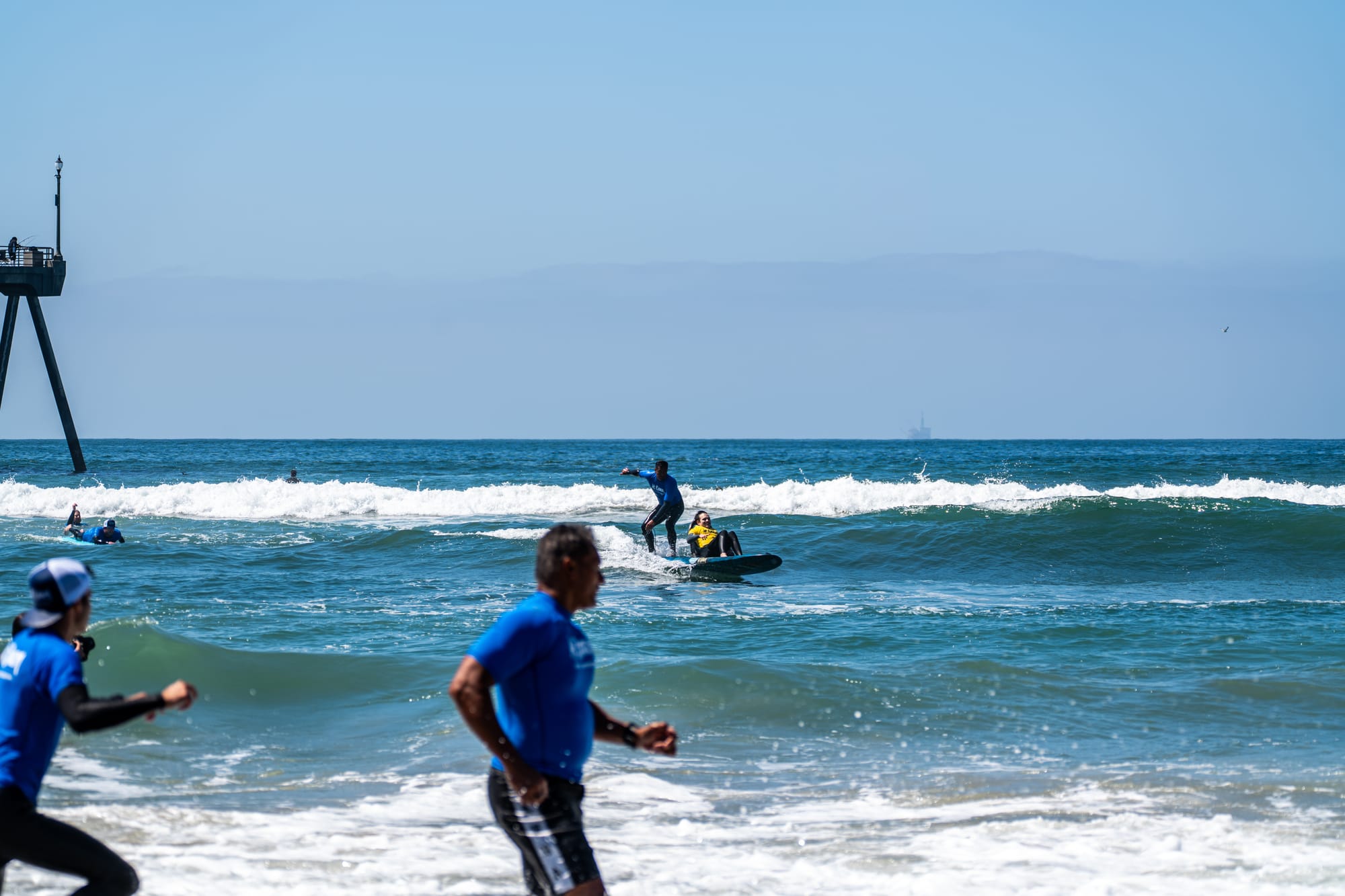Wheelchair user sitting on surf board with instructor behind him, riding a wave