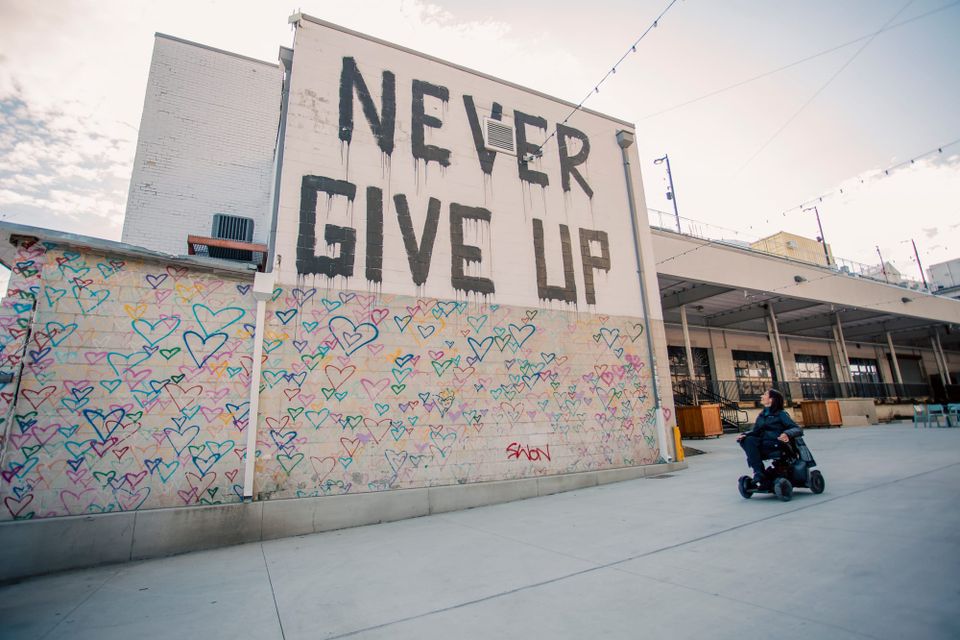 Wheelchair user in front of Washington DC's Union Market sign "Never Give Up"