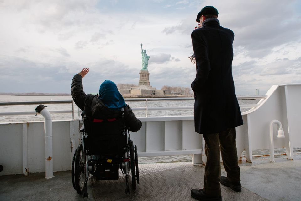 Wheelchair user and companion on an accessible ferry with Statue of Liberty in background