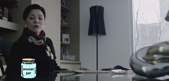 Chrisjen Avasarala sitting at her desk, looking down at her nose upon a swear jar.