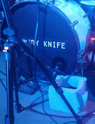 Closeup of a drumset, which is being propped up by half a cinderblock.
