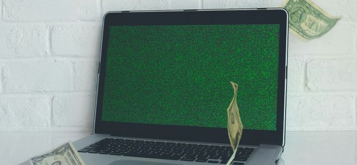 A laptop with dollar bills floating around it. The screen, also, is just green gibberish.