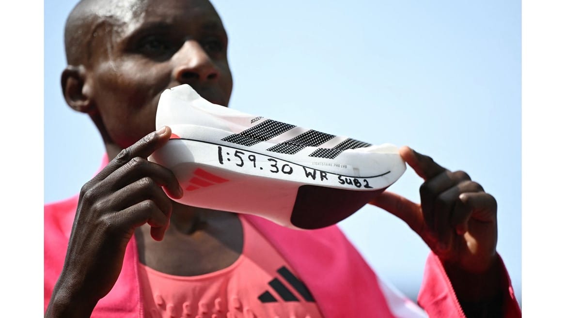 Sabastian Sawe holding up a shoe that has "1:59"30 WR SUB2" written on it.