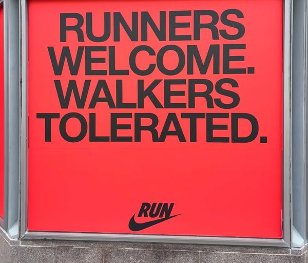 Sign with red background and black text that says "RUNNER WELCOME. WALKERS TOLERATED."