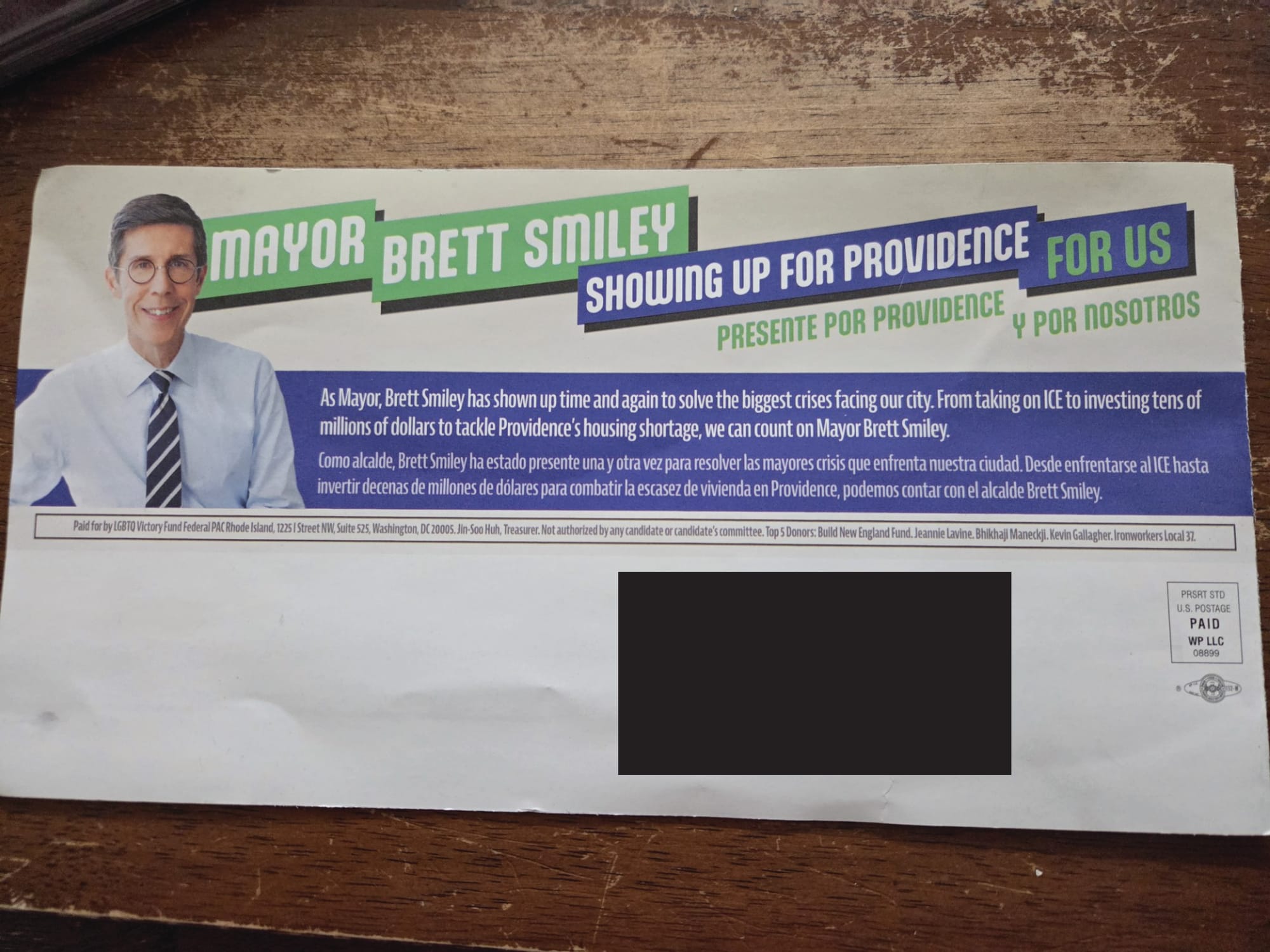 Back of mailpiece. At top, next to an image of Smiley with no background, the mailer says “Mayor Brett Smiley. Showing up for Providence for Us.” A smaller caption reads: “As Mayor, Brett Smiley has shown up time and again to solve the biggest crises facing our city. From taking on ICE to investing tens of millions of dollars to tackle Providence's housing shortage, we can count on Mayor Brett Smiley.” Both have Spanish translations. A disclosure statement below reads: “Paid for by LGBTQ Victory Fund Federal PAC Rhode Island [address], Jin-Soo Huh, Treasurer. Not authorized by any candidate or candidate's committee. Top 5 Donors: Build New England Fund, Jeannie Lavine, Bhikhaji Maneckji, Kevin Gallagher, Ironworkers Local 37. The disclosure is only in English.