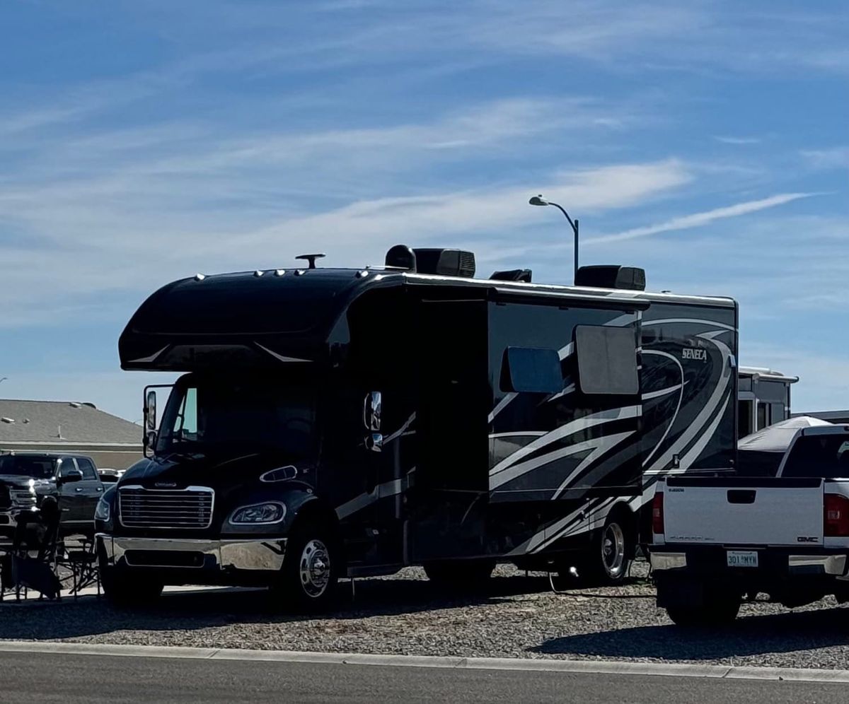 Harriet, a large Super C motorhome, parked on a gravel lot at Country Roads RV Village in Yuma, Arizona, with a pickup truck beside it.