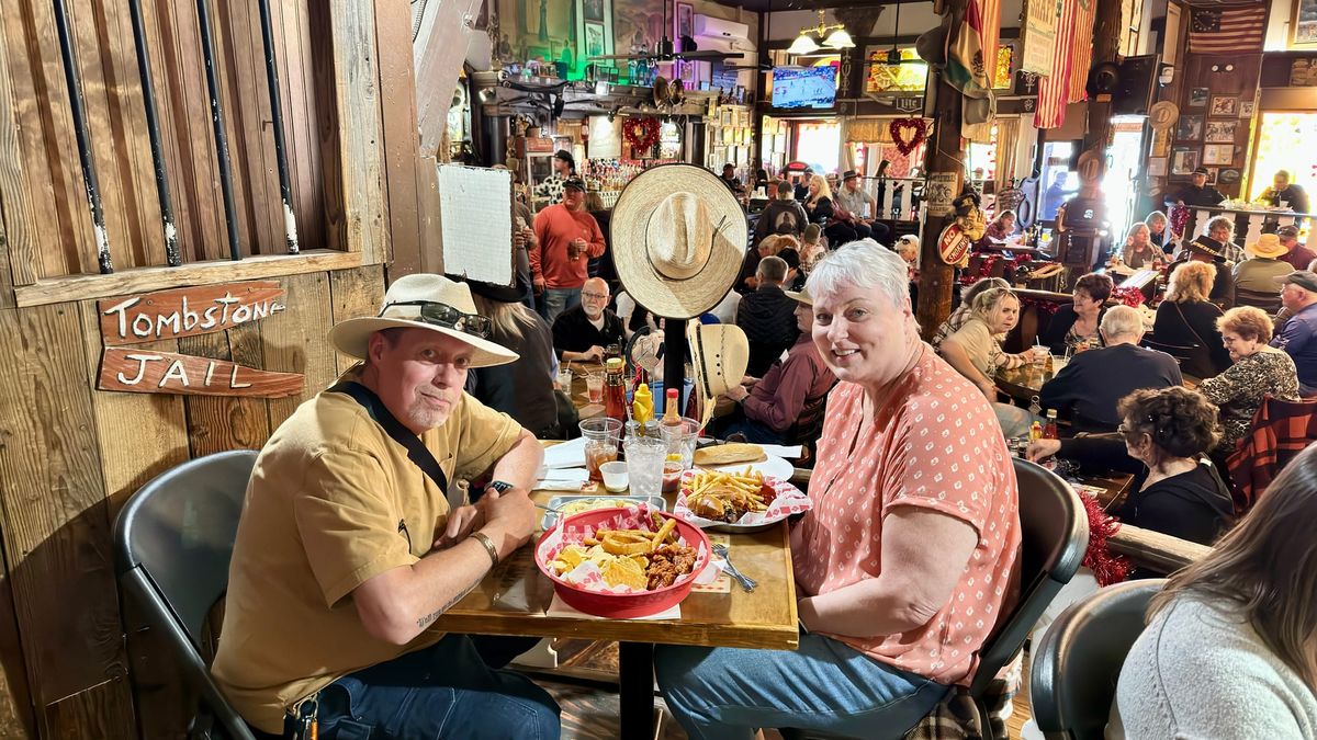 Phil and Lisa seated at a table with food inside a busy rustic restaurant in Tombstone, Arizona.