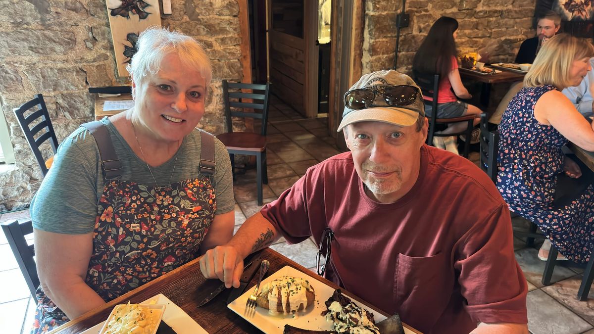 Lisa and Phil seated at a table inside Grotto in Eureka Springs, with exposed stone walls and their meal in front of them.