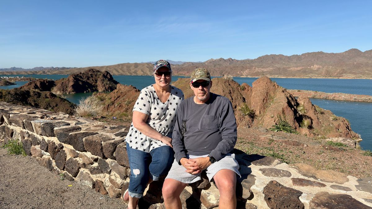 Phil and Lisa Nichols at a scenic overlook near Parker, Arizona, with desert mountains and water in the background.