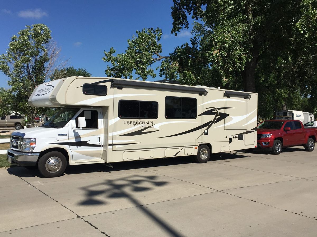 Phyllis, a cream-colored Coachmen Leprechaun motorhome, parked with a red pickup behind her.