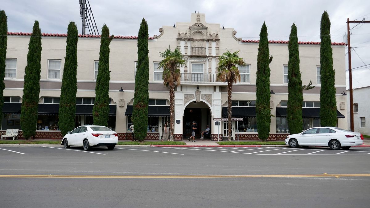 Hotel Paisano’s white facade in Marfa, Texas, with an ornate entrance, tall narrow trees and palm trees.