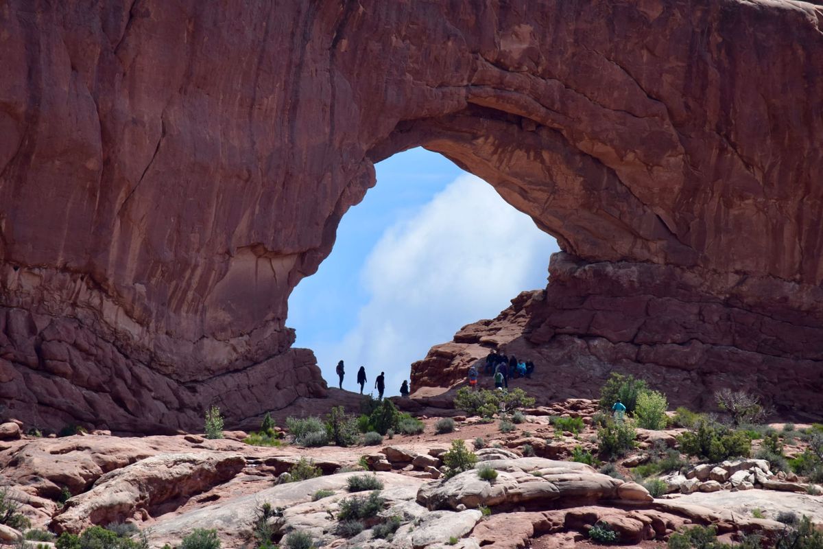 Visitors walking beneath a large red sandstone arch at Arches National Park near Moab, Utah.
